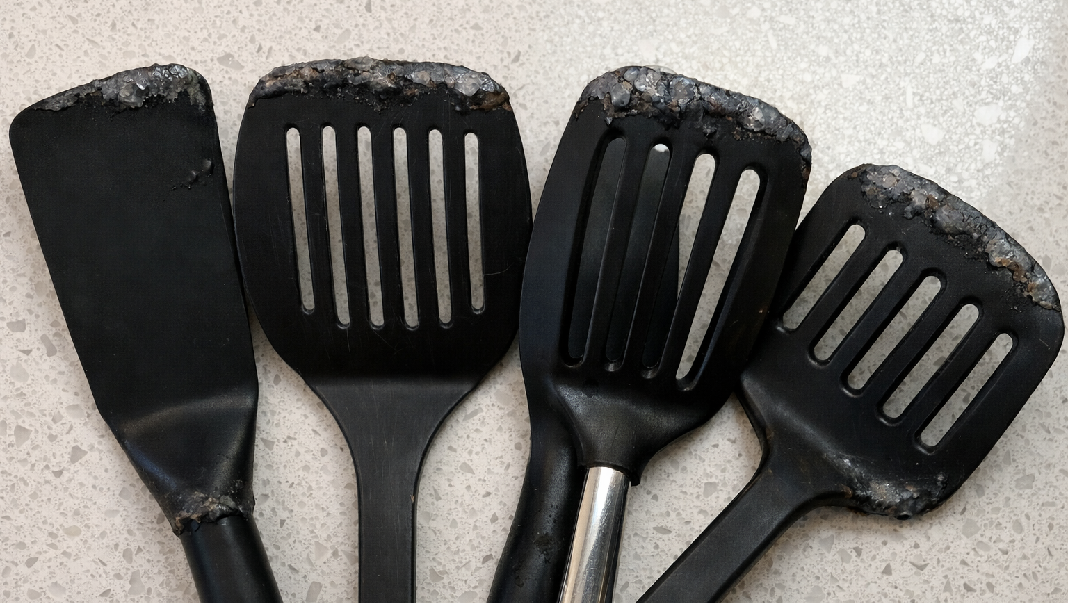 Four black spatulas with wear and residue on a light gray surface